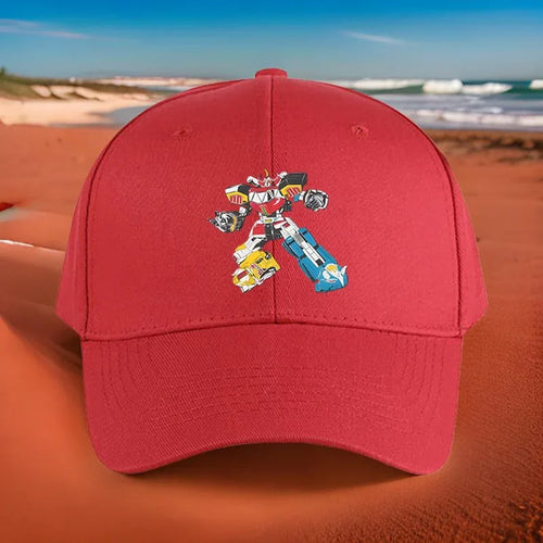 Casquette rouge avec robot coloré Megazord imprimé, posée sur une plage ensoleillée – Transformers.