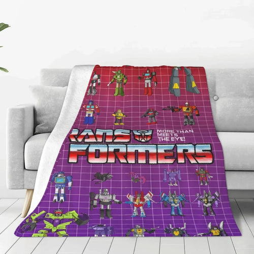 Couverture Transformers avec personnages robots colorés sur fond violet quadrillé, posée sur un canapé – Transformers.