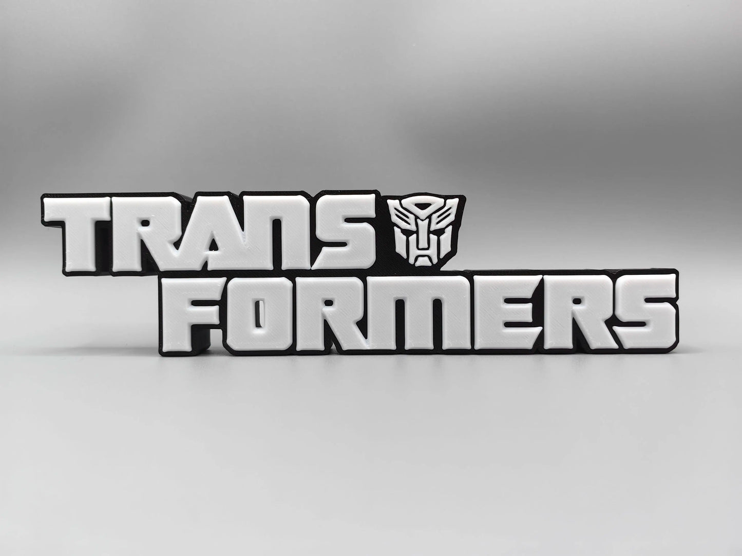 Transformers Plakette mit monochromem silbernem Logo – Metallisierte Schreibtischdekoration