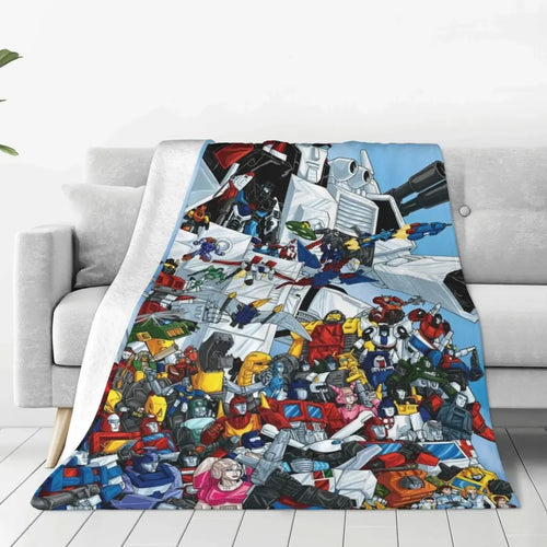 Plaid à motif Transformers, avec de nombreux robots colorés, posé sur un canapé gris – Transformers.
